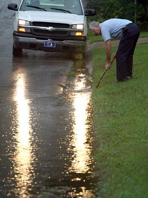 Benton street department worker Marion Orender uses a shovel to clear a plugged sewer drain along 4th Street as rain continues to fall Wednesday morning.