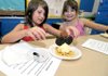 Tabitha Curlin, 9, placed cookies for the ears on her Mouse Creams as Millie Bramel, 9, giggled in the background at Glen Duffy Elementary School in Gravette on Wednesday morning. The special-treat project was a part of the school's reading program.