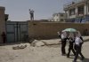 Afghan school girls chat as they pass by a house which was hit by a rocket last night, killing three family members while sleeping in their house in Kabul, Afghanistan, Monday.