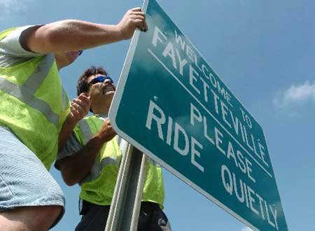 
                               
                                  Photo by Brooke McNeely&mdash;
                               
                           
                           Kevin Henson, left, and Mike Prater, with the City of Fayetteville's Transportation Department, hang one of the 6 signs around city limits that ask bikers coming to town for Bike, Blues and BBQ to ride quietly while visiting Fayetteville in 2005.