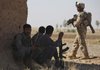 Afghan police sit in the shade as a U.S. Marine walks past during a joint patrol Tuesday in Nawa district, Helmand province in southern Afghanistan.