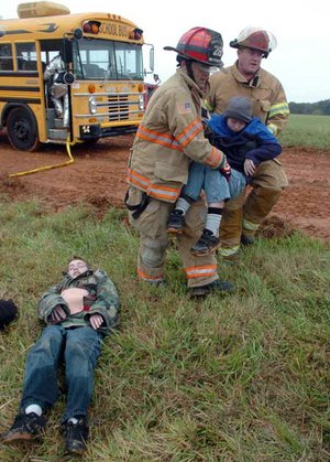 Emergency responders Blake Webb (center) from the Highfill Fire Department and Dusty Meredith from the Cave Springs Fire Department carry Luke Dunn, 11, of Springdale to lay next to David Brinkley, 12, of Gentry as they participate Saturday in a full-scale emergency exercise that simulated a plane crash at Northwest Arkansas Regional Airport.