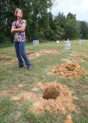 Theresa Kersey stands next to holes drilled in the ground near headstones at the Gray Cemetery north of Floyd in White County. Caretakers of the cemetery say an adjacent landowner has tried to fence off a portion of the cemetery he believes he owns.