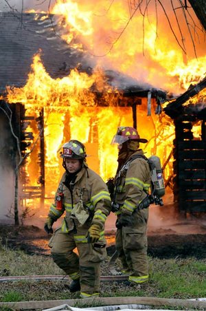 Rogers Fire Department Capt. Rob Taylor, right, and firefighter Pete Melnicki wait for water to be supplied to their hoses Wednesday at the scene of a vacant house fire on North “C” Street in Rogers. There were no injuries reported in the incident. 