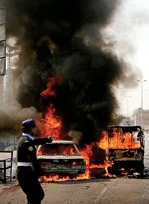A Pakistani police officer stands near burning vehicles after a suicide bombing in Peshawar, Pakistan on Monday.