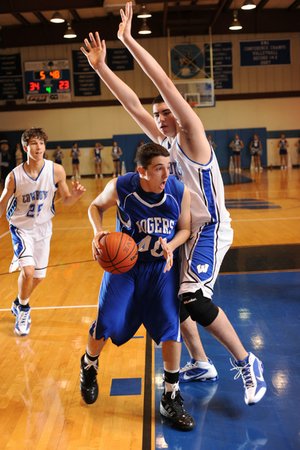 Rogers High’s Grant Holman, center, drives as Woodland’s Tyler McCullough defends during the second half of Thursday’s game at Woodland Junior High in Fayetteville.