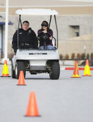 Rogers High School student Heather Gatton, 16, drives a golf cart Monday wearing “drunk goggles” with Student Resource Officer Keith Foster at Rogers High School. The goggles simulate a blood alcohol level of 0.08 to 0.15, Foster said. The exercise was sponsored by the DECA Chapter at Rogers High to remind students the effects alcohol has to impair driving and to make wise choices during holiday vacation, said teacher Tom Woodruff.