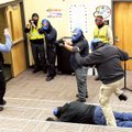 A panicked “hostage” leaps over a “body” while officers train their weapons on a “suspect” in a live...