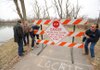 Springdale Mayor Doug Sprouse, left, and Sam Goade, director of Springdale Public Works, watch Monday as Eric Carter and Troy Lewis, right, both signs and markings technicians for Springdale, install a sign closing a portion of the walking trail at Lake Springdale along Spring Creek where erosion around the top of the lake’s levee has eroded beneath the trail.