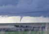 A vehicle drives across the top of Foss Lade dam with a funnel cloud in the background on March 8 in Foss Lake, Okla.