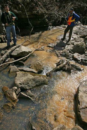 Biologist Mitch Wine (left) with the U.S. Fish and Wildlife Service and John Harris of the Arkansas Highway and Transportation Department’s Environmental Division look (left photo) Tuesday at the confluence of an unnamed tributary and Mountain Creek, noting muddy runoff coming from construction work on Arkansas 23 near Ozark. David Rickard (from left) of Fort Smith talks with Harris and Wine (right photo) about runoff on his property.