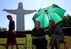 Lola Weems (middle) and her husband McKinley Weems (right) both of Eureka Springs enjoy the shade of an umbrella during the 40th Anniversary of the Dedication of the Christ of the Ozarks Statue Saturday morning at the grounds of The Great Passion Play in Eureka Springs.  Diane McClelland (far left) presented her father McKinley Weems with a miniature Christ of the Ozarks statue in recognition of his accomplishment in engineering the original statue (back left). 