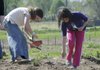 Hope Bumstead, 9, right, and Andrea Barlow, 10, plant vegetable seeds April 9 at the Gravette Gardens.