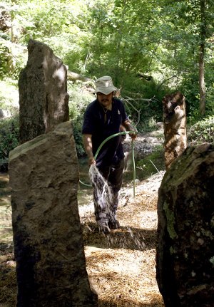 Boulder Construction employee Salvador Garcia of Bella Vista waters the area around the sculpture A Place Where They Cried after its installation Wednesday beside the walking trail at Crystal Bridges Museum of American Art in Bentonville.
