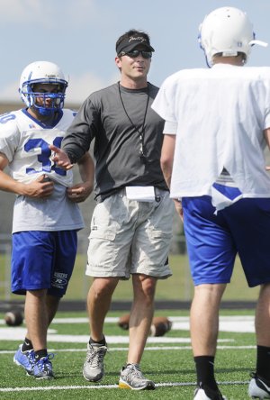 Rogers High football coach Shawn Flannigan, middle, speaks to Nick Wary, right, at practice Monday in Mountie Stadium in Rogers.