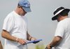 Rogers High assistant coach Cam Prock, left, looks over notes at practice Monday in Rogers.