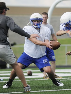 Rogers High’s Nick Wary hands off the ball during Monday’s practice in Mountie Stadium in Rogers.