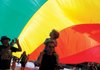 Ben Buonaiuto and his son Ari Buonaiuto, 4, walk under a large flag down Dickson Street during the Pride Parade Saturday in Fayetteville. The pair joined hundreds of participants and spectators for the parade, which ended with a brief rally in the parking lot of the Walton Arts Center.