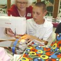 Hariet Mack helps Spencer Mortimeyer sew a cloth bag Tuesday during the annual All-Church Sewing Bee...