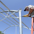 GREENHOUSE GROUNDWORK - Ken Dawson, with Bentonville Parks Department, drills a bolt into the brace ...