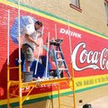 Muralist Chuck Bame pieces together plastic pipe Sunday to make an awning to shade his work on a Coc...