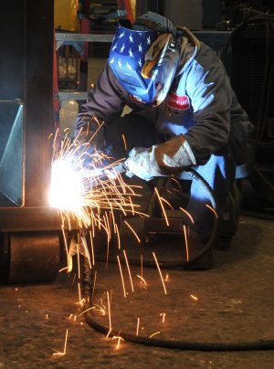 Beningo Barron welds a compactor Thursday evening at the Cram-A-Lot plant in Springdale.