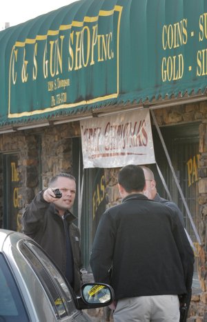Springdale police detective Michael Hendrix talks to fellow detective Ben Townsend and Lt. Kevin Lewis on Tuesday about the shooting scene at C&S Gun Shop on Thompson Street in Springdale.