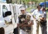 Clayton Morgan, director of the Humane Society for Animals in Rogers, carries a handful of puppies found Thursday inside a mobile home in Centerton to the shelter as John Newell, right, animal control deputy, and Capt. Mike Jones with the Benton County Sherriff’s Office, talk in Rogers. To see more photos visit http:// photos.nwaonline.com.
