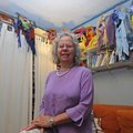 Jo Ann Kaminsky stands under some of the masks she has created at The Art Experience in Fayetteville...