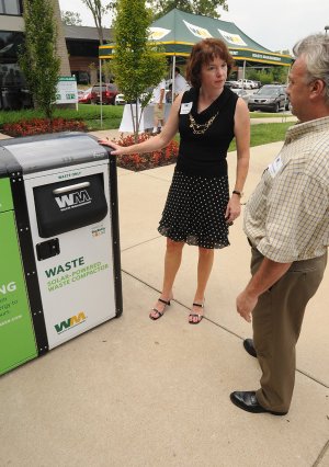 Nancy Woods explains the use of a solar-powered compactor to Richard Massey during a grand opening Tuesday for Waste Management’s Sustainability Center in Rogers. The compactor compresses nonrecyclable waste and is paired with a bin for recyclables.