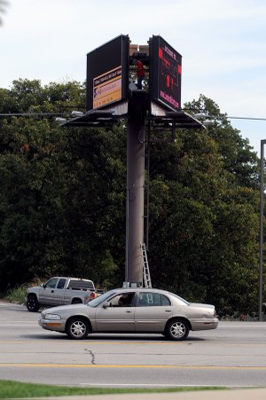 SIGN OF THE TIMES An employee of Ashby St. Outdoor makes adjustments earlier this week to a digital billboard near the boundary between Springdale and Fayetteville. Springdale doesn’t allows new billboards but allows existing boards to be upgraded. Fayetteville has prohibited billboards for about 40 years and Rogers nixed them in the early ’90s. Bentonville allows digital boards if old, static boards are removed in exchange.
