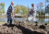 Bruce Combs, left, and Terry Arnold, both inmates, fill in a trench Monday where the two, along with fellow inmates, had been working to put in a new culvert between two ponds at the Benton County Sheriff’s Office. The culvert will be used to level out the water levels in the ponds, which will be used to irrigate a garden being built on the property.