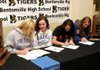 Melissa Bakke, left, signs with John Brown University, Rebecca Brown with Drake University, Shayne Wiedemann with Pittsburg State University and Kelsey Parks with the University of Tulsa. Flanked by 2010 and 2011 7A State Championship trophies, Bentonville Lady Tigers Volleyball scholarship winners sign on Tuesday to play for four universities.