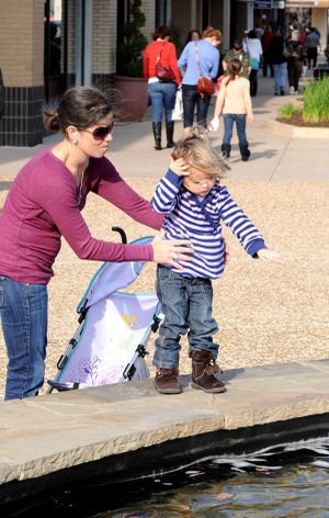 MAKE A WISH Cristina Harbaugh holds daughter Audra Harbaugh, 2, while she tosses a coin in a fountain at Pinnacle Hills Promenade for a holiday wish in Rogers. The two were among the crowds of shoppers to visit retailers on “Black Friday,” traditionally the busiest day of the year for retailers.
