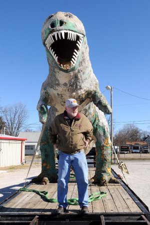 Sam Hawkins stands with his Tyrannosaurus Rex before a crew unloads it at Sam’s Olde Tyme Hamburgers in Rogers on Monday. Hawkins plans to restore the dinosaur and put it on display near the restaurant.