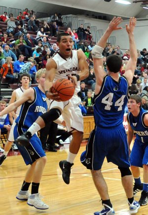 Tony Dennis, Springdale High senior, leaps around Rogers High senior Nathan Musso, right, while driving to the basket during the first half Friday at Bulldog Gym in Springdale.
