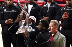 Arkansas football players Cobi Hamilton and Tenarius Wright (center) and Coach Bobby Petrino hold up the Cotton Bowl trophy during halftime of Arkansas’ basketball game against Michigan on Saturday at Walton Arena in Fayetteville. 