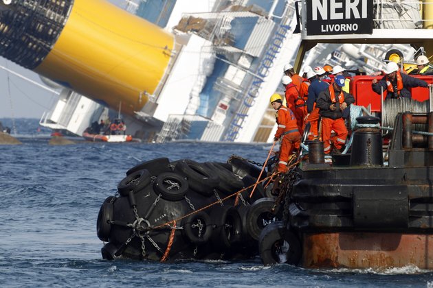 experts-aboard-a-sea-platform-carry-oil-recovery-equipment-as-they-return-to-the-port-of-the-tuscan-island-of-giglio-italy-where-the-cruise-ship-costa-concordia-visible-in-background-ran-aground-saturday-jan-28-2012-rough-seas-off-italys-tuscan-coast-forced-a-delay-in-the-planned-saturday-start-of-the-operation-to-remove-a-half-million-gallons-of-fuel-from-the-grounded-costa-concordia-and-officials-said-pumping-may-now-not-begin-until-midweek