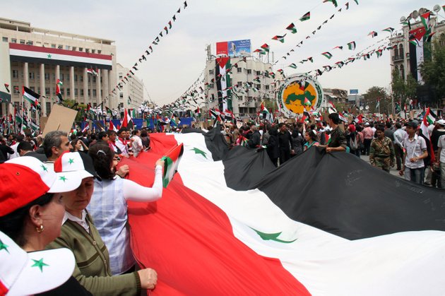 pro-syrian-government-demonstrators-carry-a-giant-national-flag-at-a-rally-at-sabe-bahrat-square-to-commemorate-the-65th-anniversary-of-the-foundation-of-the-ruling-baath-arab-socialist-party-in-damascus-syria-saturday-april-7-2012-syrian-president-bashar-assad-has-accepted-a-cease-fire-deadline-brokered-by-international-envoy-kofi-annan-which-calls-for-his-forces-to-pull-out-of-towns-and-cities-by-tuesday-and-for-both-government-and-rebels-to-lay-down-their-arms-by-6-am-local-time-thursday