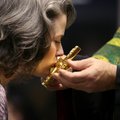 Leslie Pappas of Rogers leans in to kiss a cross held by Father John Maxwell during a vespers servic...