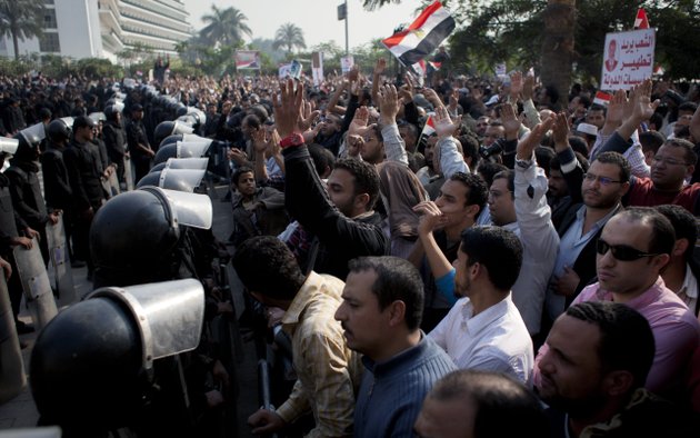 supporters-of-egyptian-president-mohammed-morsi-chant-slogans-as-riot-police-left-stand-guard-in-front-of-the-entrance-of-egypts-top-court-in-cairo-egypt-sunday-dec-2-2012-egypts-top-court-announced-on-sunday-the-suspension-of-its-work-indefinitely-to-protest-psychological-and-physical-pressures-saying-its-judges-could-not-enter-its-nile-side-building-because-of-the-islamist-presidents-supporters-gathered-outside-arabic-on-the-poster-right-reads-the-people-want-to-purify-the-states-institutions