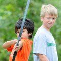 Griffin Roton, 10, right, watches as Keeno Ghadbin, 9, aims his bow and arrow at a target Wednesday,...
