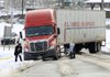 Truckers Michael Wells (left) and C’rone Hill try to dig snow and ice from underneath the wheels of their tractor-trailer Thursday morning after sliding off Kanis Road in Little Rock. 