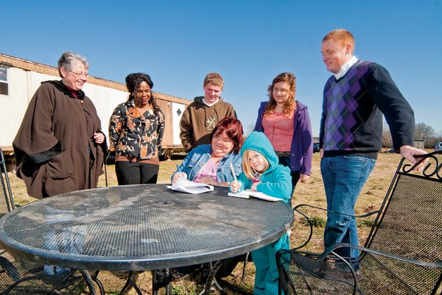 standing-from-the-left-robin-richards-shenel-sandidge-caleb-price-caitlin-price-and-danny-smith-pastor-of-crosspoint-baptist-church-watch-as-amy-price-signs-paperwork-for-ownership-of-a-soon-to-be-renovated-trailer-cacie-skidmore-4-amys-daughter-draws-while-the-signing-takes-place