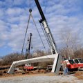 Workers hoist the first of three concrete bridge sections into place Wednesday that span a creek alo...