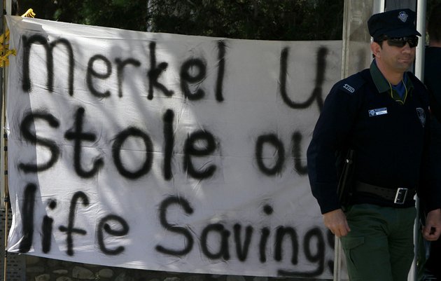 a-police-officer-stands-by-a-protest-banner-outside-of-parliament-before-a-meeting-in-capital-nicosia-cyprus-on-monday-march-18-2013