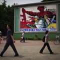 People walk past a roadside propaganda billboard promoting the "military first" policy and a boost t...